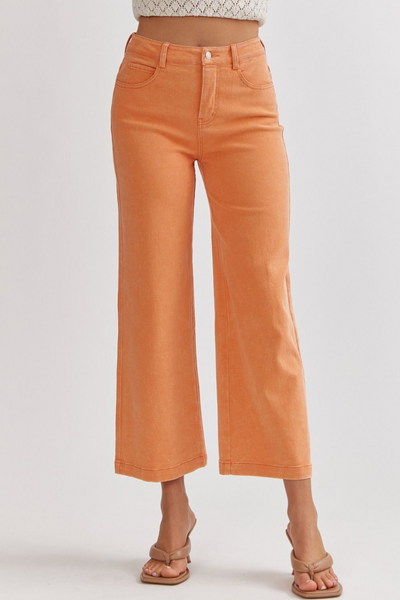 A model wearing high-waisted orange acid wash wide leg pants with zipper front closure and pockets.