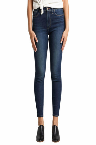 A person standing wearing dark indigo high-rise skinny jeans and black ankle boots.